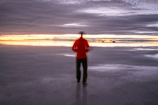 istock Person in Red Jacket Standing on Reflective Salt Flats at Sunrise 2201820683
