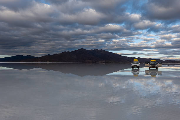 Two off-road vehicles on reflective salt flats under dramatic clouds. Adventurous journey in remote terrain. Scenic outdoor exploration.