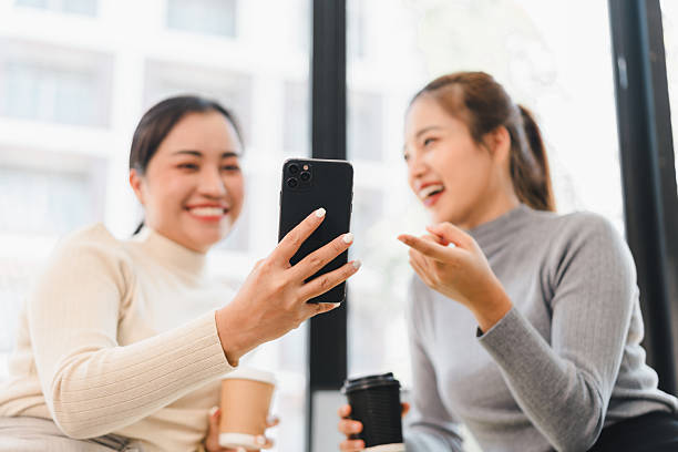 istock Two women smiling while looking at smartphone and holding coffee 2201826752