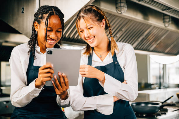 istock Two famous chefs discussing their video blog in a professional stainless steel kitchen using a tablet. Professionals smiling reading searching communicating with modern technology. 2201828450