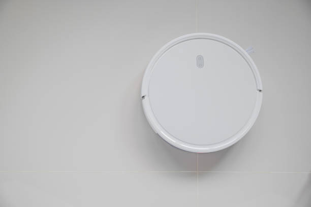 istock White automatic floor cleaner with side brush on tile flooring. Top view of robot vacuum cleaner removing dust, showcasing modern smart home cleaning technology for spotless 2201828555