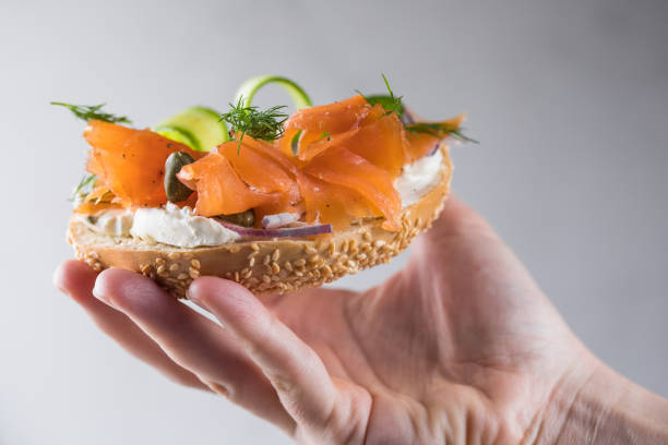 istock Girl Putting a sandwich for breakfast. Bagel with cheese, cucumber,  red fish. 2201828628