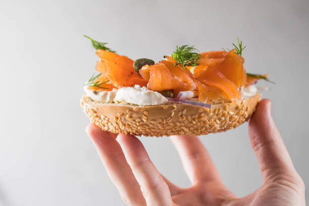 istock Girl Putting a sandwich for breakfast. Bagel with cheese, cucumber,  red fish. 2201828638