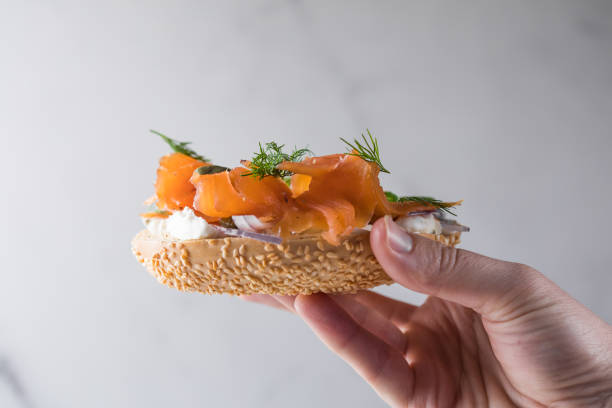istock Girl Putting a sandwich for breakfast. Bagel with cheese, cucumber,  red fish. 2201828639