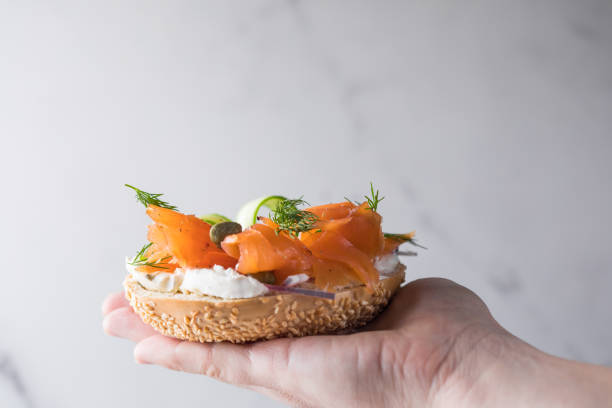 istock Girl Putting a sandwich for breakfast. Bagel with cheese, cucumber,  red fish. 2201836317