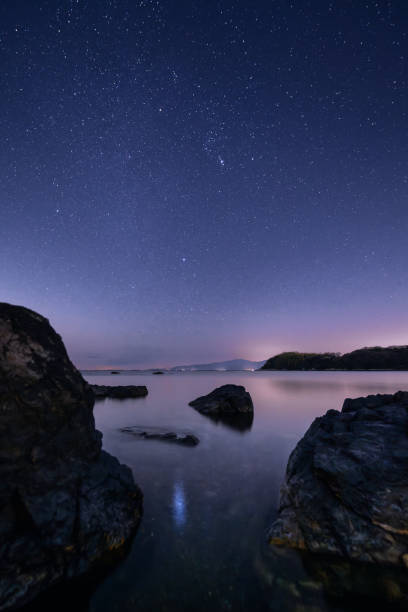Star filled night sky above the sea with a rocky coastline