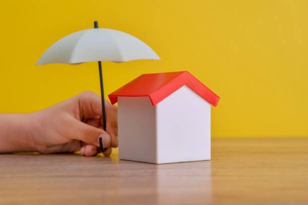 istock A toy house is being sheltered by a miniature umbrella held by a hand. 2201840804