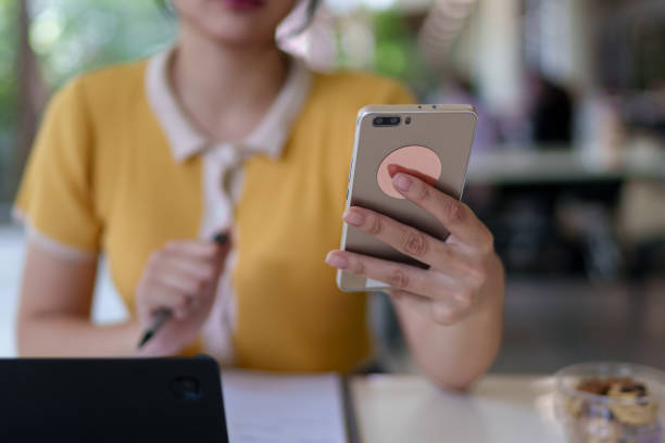 istock Young Asian woman using a smartphone while studying with a tablet in a university cafe, with books and a drink on the table 2201844754