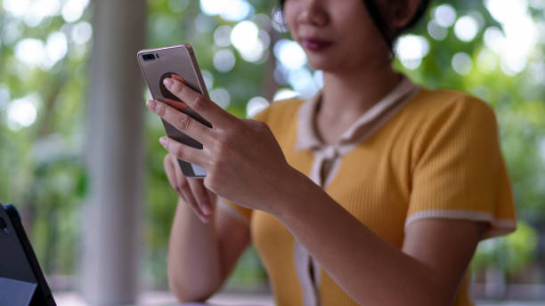 istock Young Asian woman using a smartphone while studying with a tablet in a university cafe, with books and a drink on the table 2201844768