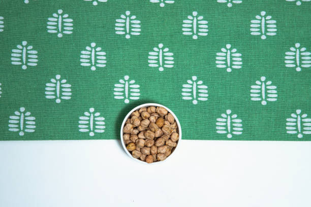 istock This image showcases a white ceramic bowl filled with dried chickpeas, placed on a clean white surface with a green, patterned cloth backdrop. 2201845503
