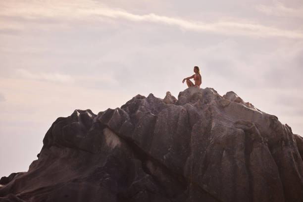 Young carefree woman day dreaming while relaxing on a rock against the sky. Copy space.