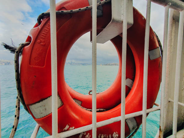 A bright orange lifebuoy on a ferry railing frames the Bosphorus, with Istanbul's skyline in the background