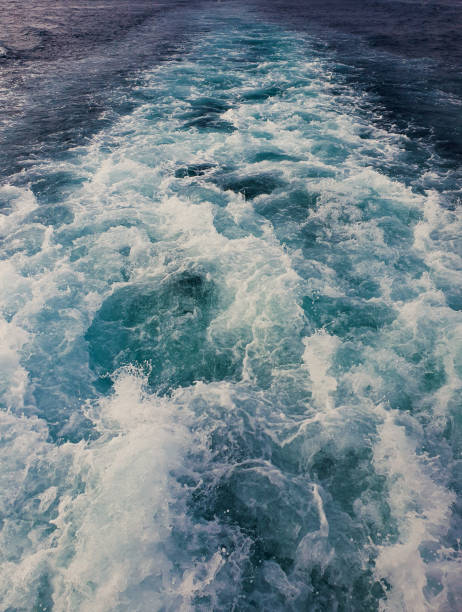 Foamy ocean waves trailing behind a moving boat, creating a vibrant mix of deep blue and turquoise water patterns