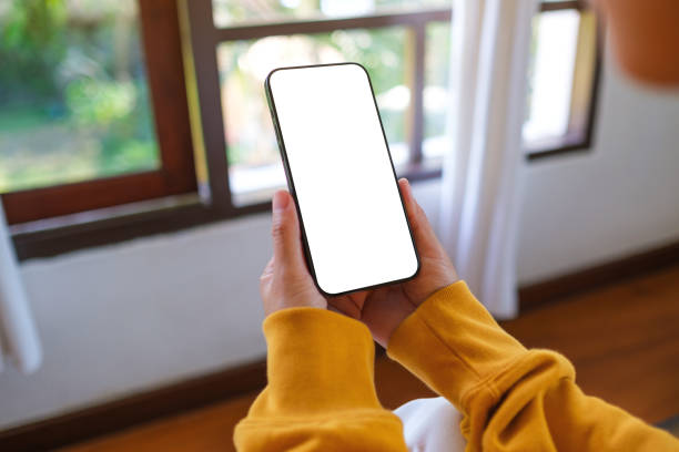 istock Mockup image of a woman holding mobile phone with blank desktop screen while sitting in bed room at home 2201853619