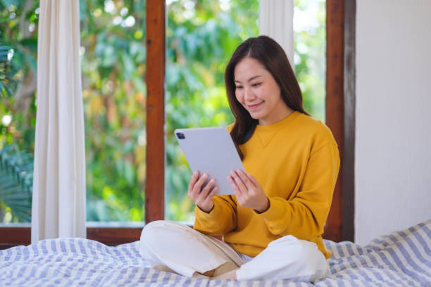 istock Portrait of a woman holding and using digital tablet while sitting on bed 2201853667