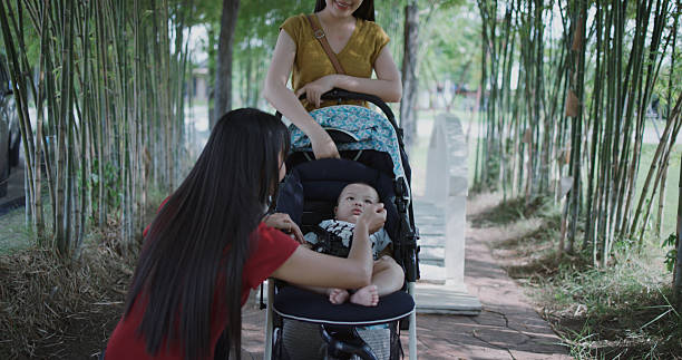 Young mother walking in a park with children in pushchair. Mom and kids in a buggy walk in forest. Woman pushing a double stroller for twin boy and girl and newborn baby. Active family outdoors.