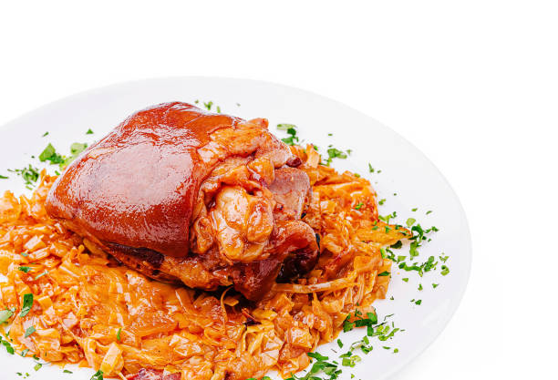 Hearty pork knuckle is plated atop a bed of seasoned and sautéed cabbage, garnished with fresh herbs. The dish showcases a rich, inviting appearance, perfect for a comforting meal.