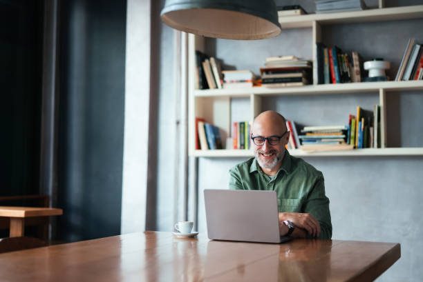 Smiling Man Working on Laptop in Modern Workspace with Bookshelves