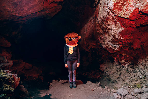 person wearing a large bear mask and formal clothing standing in a dimly lit cave, creating a surreal and eerie scene