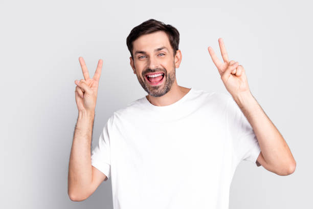 istock Happy young man wearing white t-shirt showing peace hand gestures with both hands against light background 2201864244