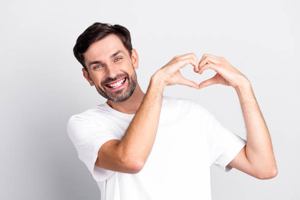 istock Smiling young bearded man making heart shape with hands dressed in casual style against a light grey background 2201864291