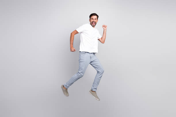 istock Excited young man jumping with a joyful pose in casual outfit against a grey background, expressing happiness and energy. 2201864439