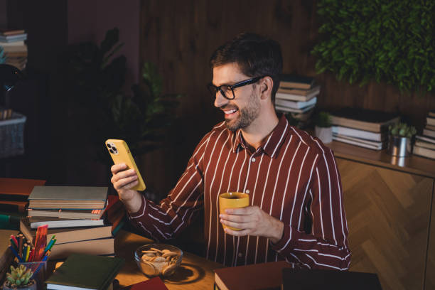istock Young man in casual shirt multitasking at home, using smartphone with yellow cover and enjoying coffee 2201866845