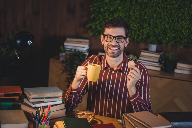 istock Young man enjoying tea and snacks while studying books late at home, surrounded by comfort and leisure 2201866846