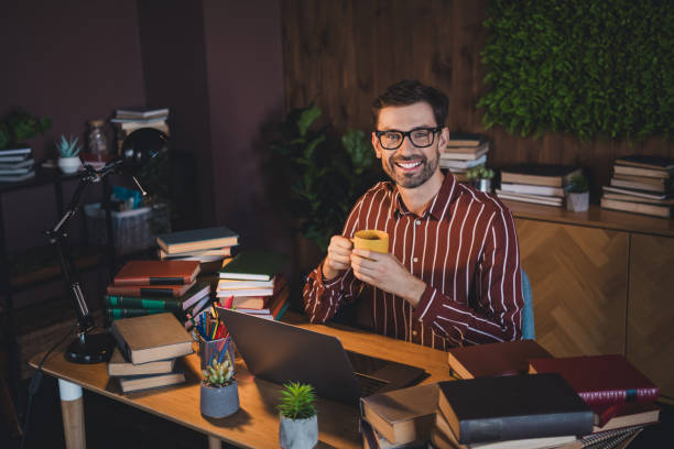 istock Smiling young man enjoying leisure time studying at home office surrounded by books, holding coffee 2201866928