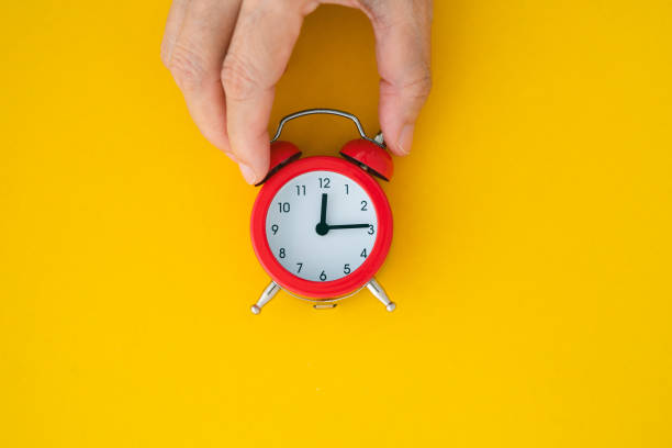 istock Hand holding red analog alarm clock on yellow background, top view 2201867672