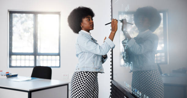 Teacher, black woman and smart board in classroom for explaining rules, exam and math education. Digital, writing and stylus with tech, lecturer and equations in university for degree in physics