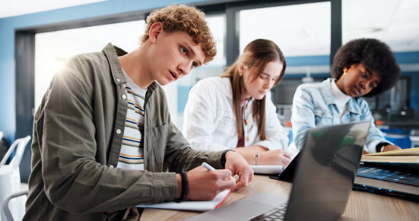istock Studying, group and students with laptop, classroom and research for assignment in college or writing. Education, learning and people with tech for knowledge, university and teamwork for project 2201869902