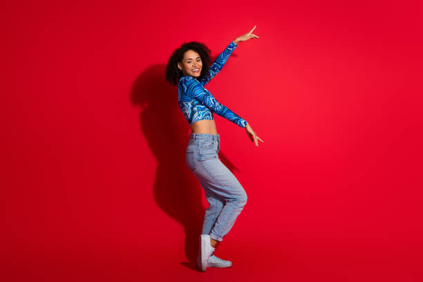istock Young woman in a blue patterned top and jeans posing excitedly against a bright red background, exuding cheerful vibes 2201871215