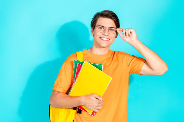 istock Young male student smiling confidently while holding notebooks against a vibrant teal background 2201871678