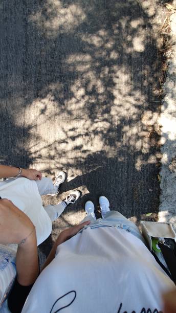 Two girl couples walking down the street, beautiful weather sunlight casting tree shadows that sway with my steps. afternoon, viewed from above, taking a selfie, my feet, human legs, foot, shoes