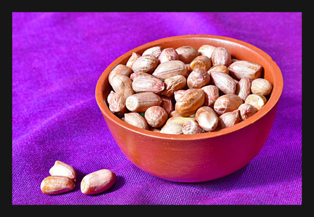 Raw peanuts in a clay bowl, with a purple plain fabric background, Pune, Maharashtra, India.