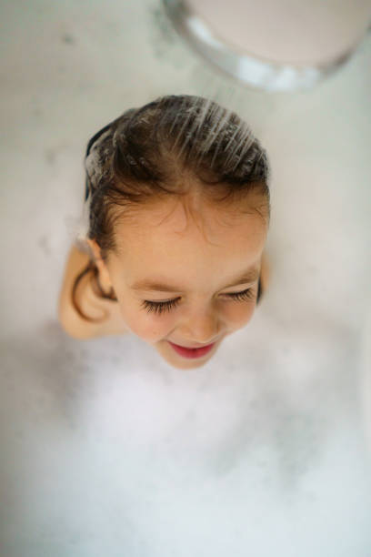 Cute happy girl washes her hair while sitting in a bathtub