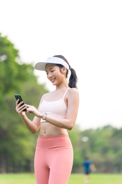 istock Young Asian Woman with Visor Cap Using Phone While Exercising Outdoors In a Park 2201879114