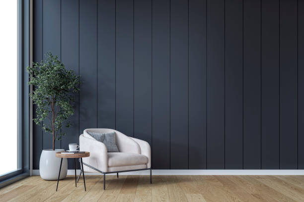 A minimalistic, unfurnished interior with a cozy armchair, side table  and potted plant in front of an empty black paneled accent wall background with copy space, and a window