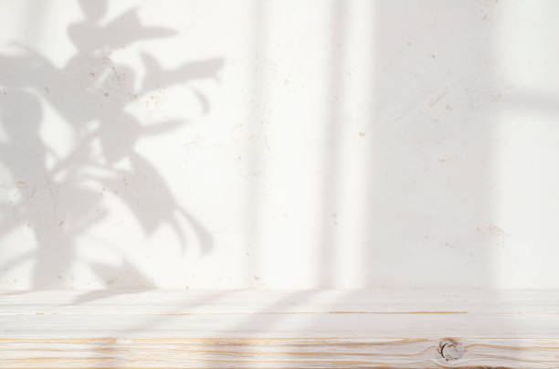 istock Blur cream white cement wall with soft beautiful dappled sunlight leaves shadows background for product presentation on in focus wooden table 2201881760