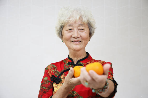 Portrait of an Asian senior woman holding tangerine dressed in traditional Chinese attire