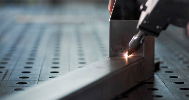 Close-up view of aluminum welding with a precision tool, featuring a metallic workpiece and a controlled laser beam on a perforated surface.