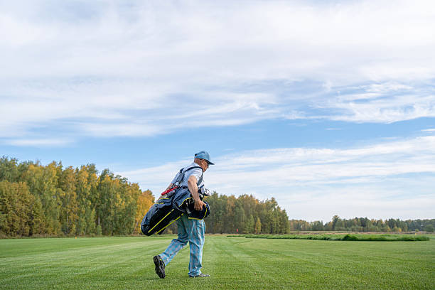 A man carrying his golf clubs and other equipment walks leisurely across a beautiful lush green golf course