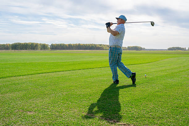 Asian elderly man golfer playing a fairway shot on a sunny golf course surrounded by nature. Perfect scene for golf, outdoor sports, active lifestyle, leisure, fitness, recreation and concepts.