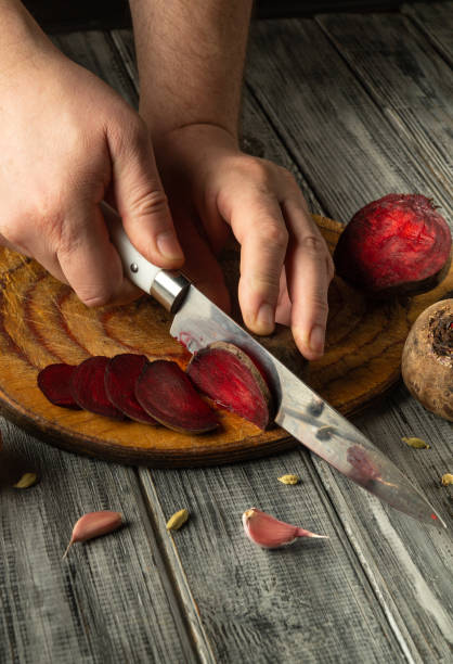 istock Hands skillfully cut vibrant red beets into thin slices on a rustic wooden cutting board. Surrounding ingredients include garlic cloves, adding flavor to the preparation 2201898271