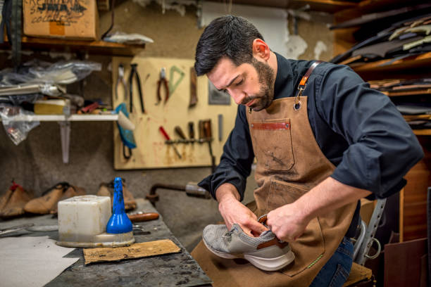 istock Skilled cobbler working carefully on worn gray shoe, surrounded by leather-working tools in rustic workshop, showcasing traditional shoe repair artistry 2201899442