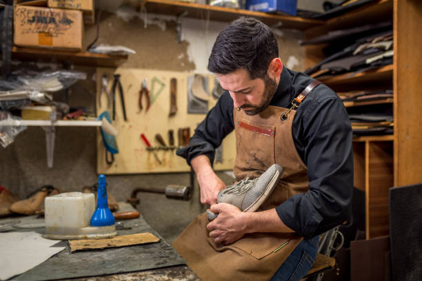 istock Skilled artisan working on shoe repair, wearing leather apron in traditional workshop, surrounded by cobbler's tools and crafting materials 2201899455