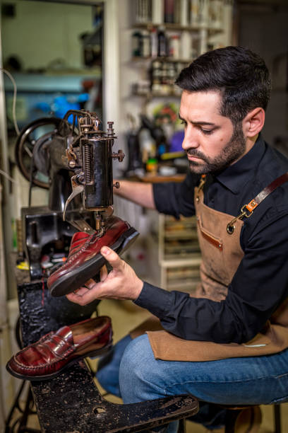 istock Experienced shoemaker repairing leather loafer on vintage sewing machine, highlighting skilled handcrafting techniques in traditional workshop setting 2201900718