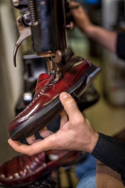 istock Skilled cobbler's hands mending vintage red leather shoe on traditional sewing machine, highlighting artisanal leather repair technique 2201900728