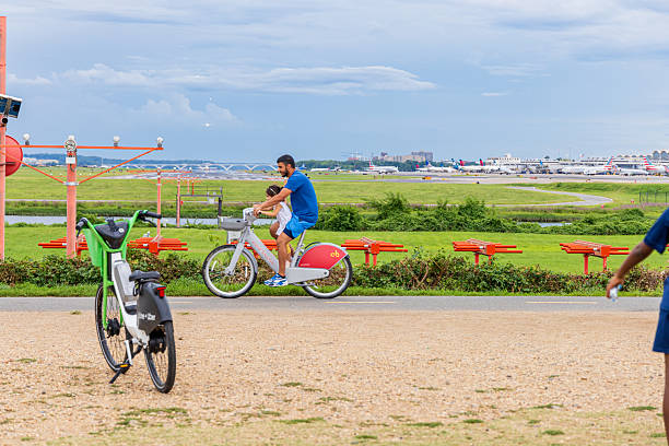 Washington, DC. USA - Ago 19th 2024: A man and a child ride a bicycle in Gravelly Point, Washington. There are several other bicycles in the park, including one that is parked near a bench. The park is located near an airport